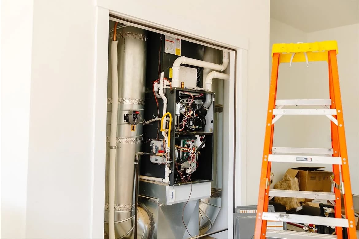 Open furnace installation in a closet beside a yellow ladder