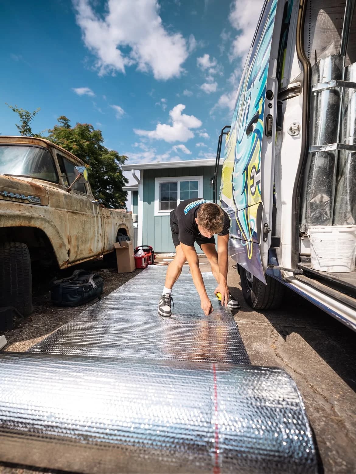 Technician measuring reflective duct insulation beside a service van
